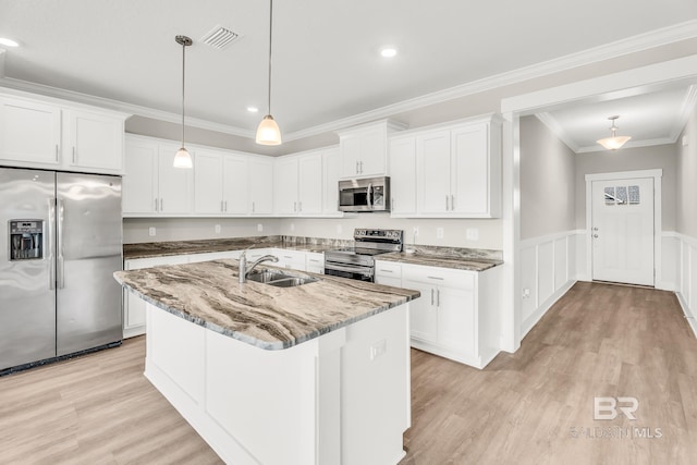 kitchen featuring appliances with stainless steel finishes, white cabinetry, hanging light fixtures, and an island with sink