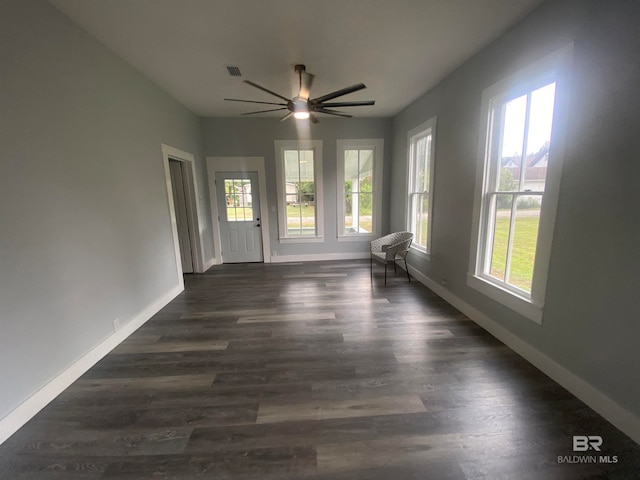 empty room with a healthy amount of sunlight, ceiling fan, and dark hardwood / wood-style floors