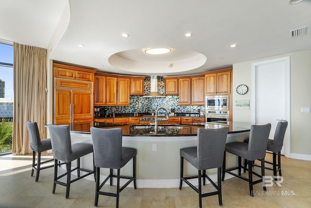 kitchen with built in appliances, visible vents, backsplash, wall chimney exhaust hood, and a tray ceiling