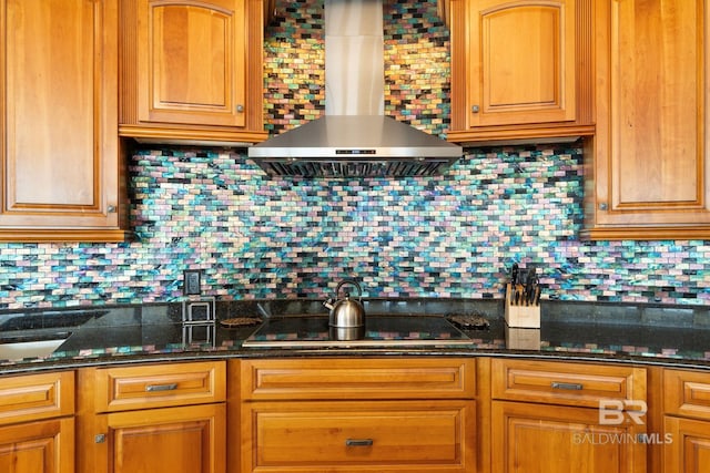 kitchen with wall chimney range hood, black electric stovetop, decorative backsplash, and dark stone countertops