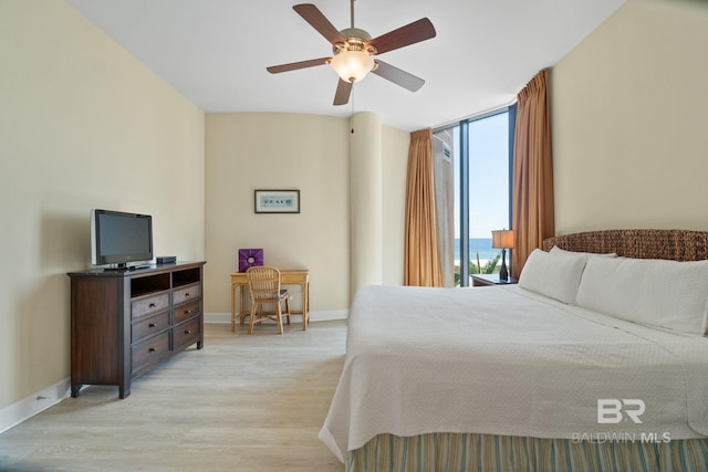 bedroom featuring expansive windows, light wood finished floors, a ceiling fan, and baseboards