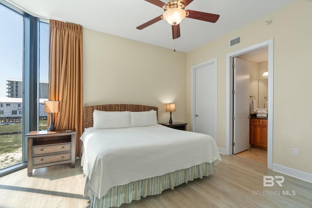 bedroom featuring connected bathroom, light wood-style flooring, visible vents, baseboards, and expansive windows