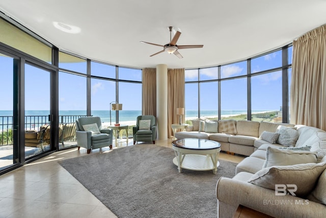 tiled living room with ceiling fan, a wall of windows, and a water view