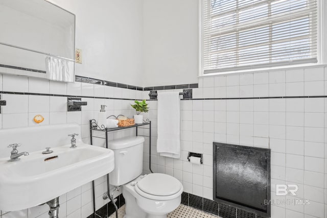 bathroom with tile walls, toilet, a wainscoted wall, and a sink