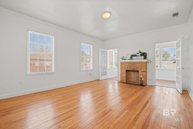 unfurnished living room with a brick fireplace, visible vents, a wealth of natural light, and light wood-type flooring