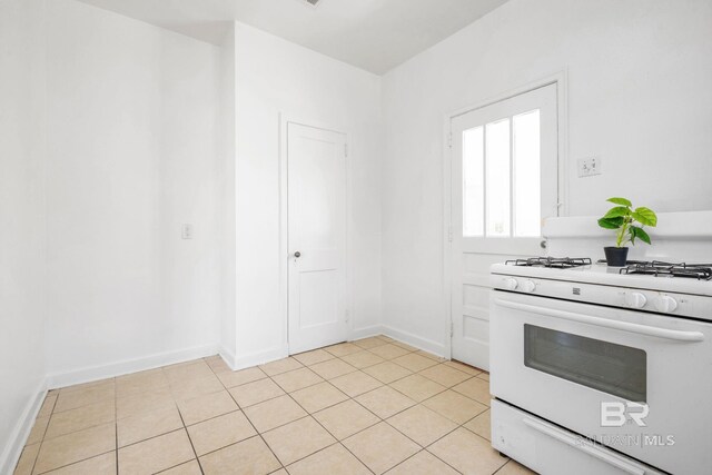 kitchen with white gas range, light tile patterned floors, and baseboards