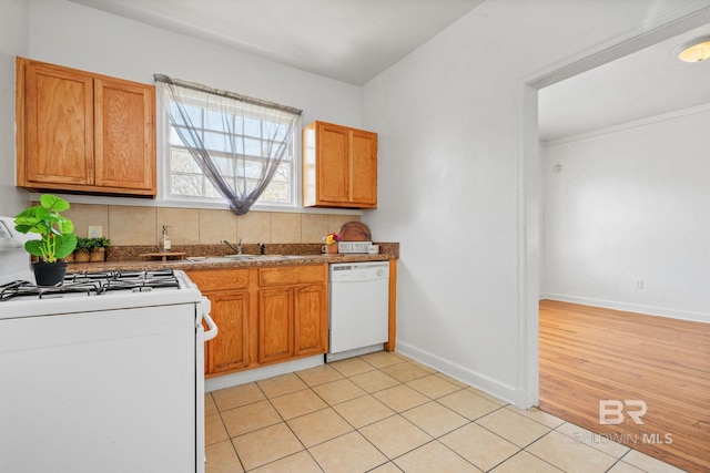 kitchen with brown cabinets, a sink, white appliances, light tile patterned floors, and baseboards