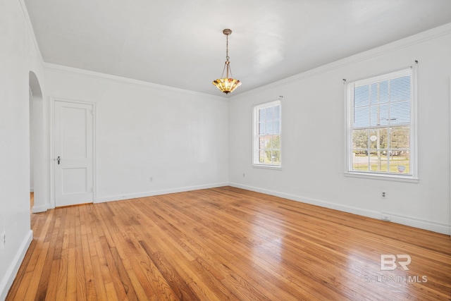 unfurnished room with arched walkways, light wood-style flooring, baseboards, and ornamental molding