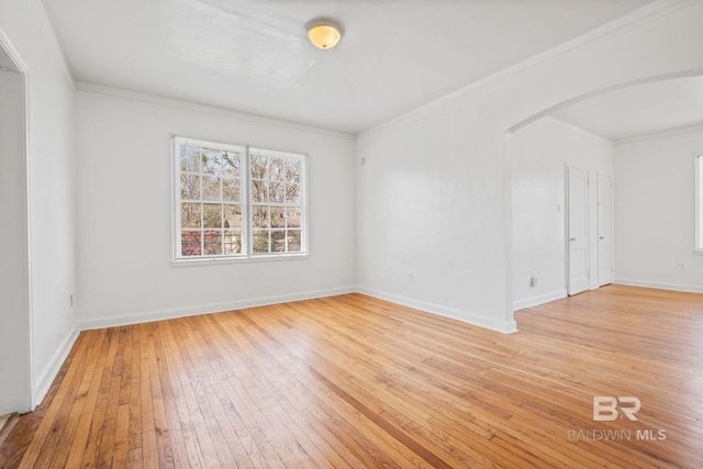 empty room with ornamental molding, baseboards, arched walkways, and light wood-type flooring