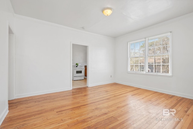 empty room featuring crown molding, light wood-type flooring, and baseboards