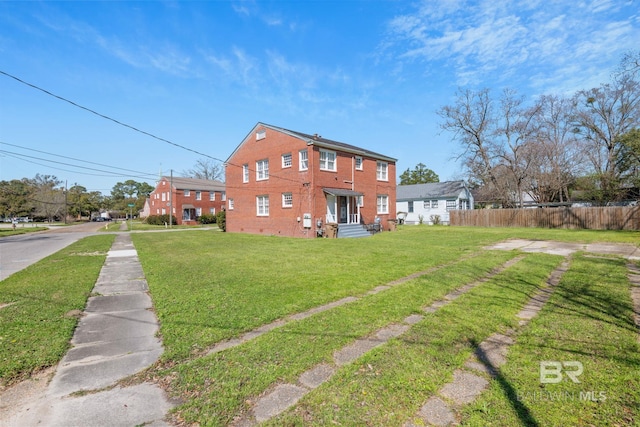 back of house featuring brick siding, a lawn, and fence