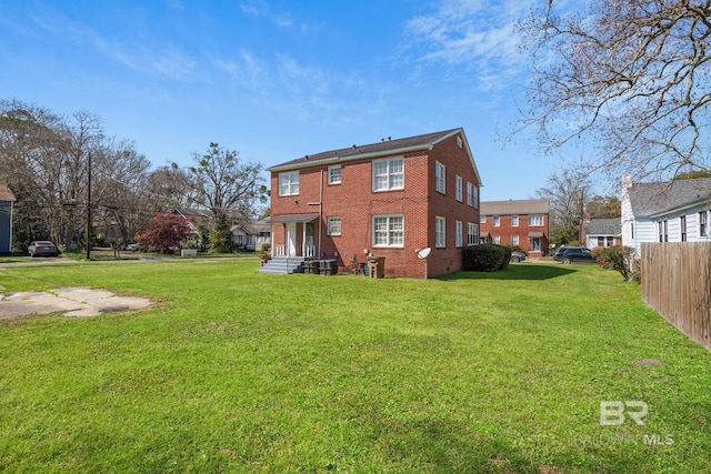 rear view of house featuring brick siding, a yard, and fence