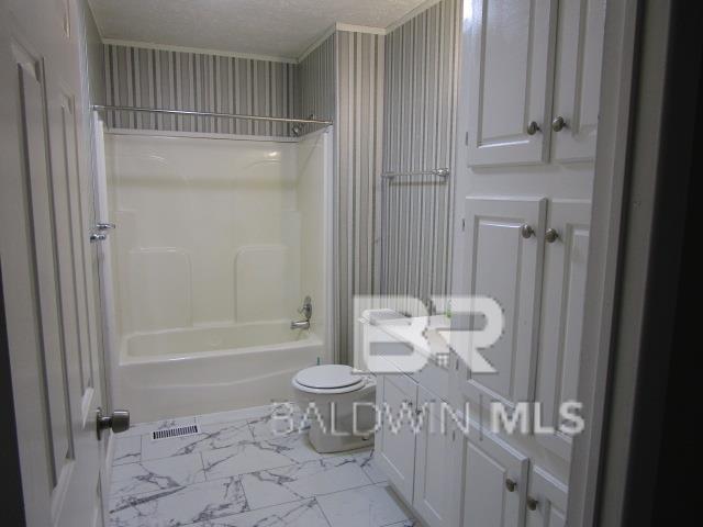 bathroom with a textured ceiling, marble finish floor, tub / shower combination, and toilet