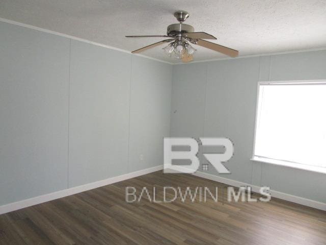 empty room with ornamental molding, dark wood-type flooring, and baseboards