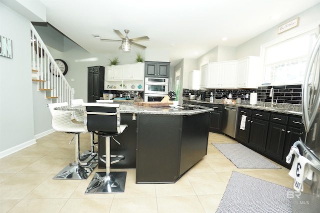 kitchen with ceiling fan, a center island, stainless steel appliances, white cabinets, and light tile patterned flooring