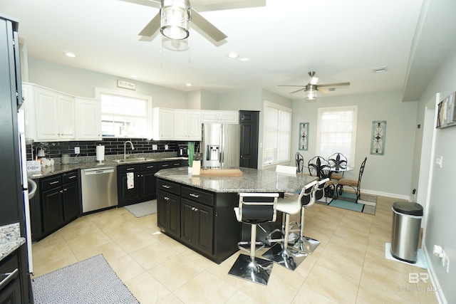 kitchen with stone counters, a center island, a kitchen breakfast bar, white cabinets, and appliances with stainless steel finishes