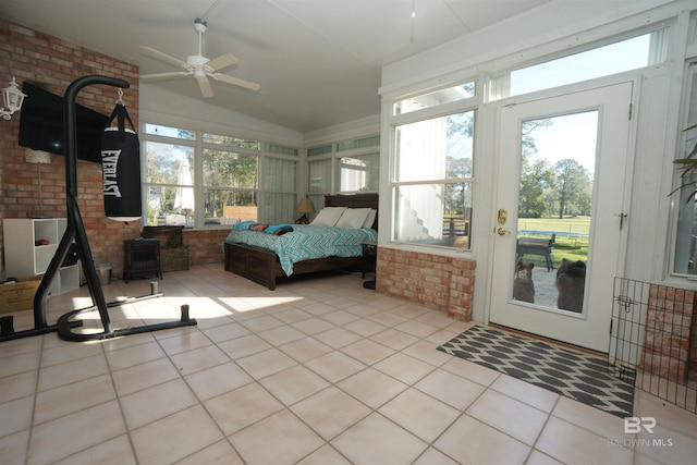 tiled bedroom featuring ceiling fan, vaulted ceiling, multiple windows, and brick wall