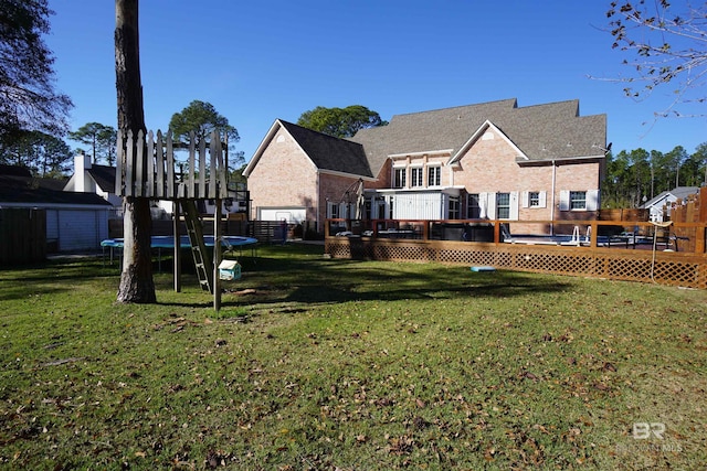 rear view of property featuring a trampoline, a yard, and a wooden deck