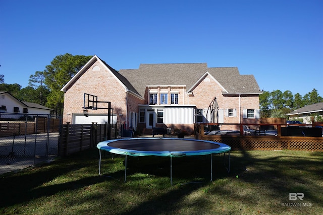 back of house featuring a trampoline, a deck, and a lawn