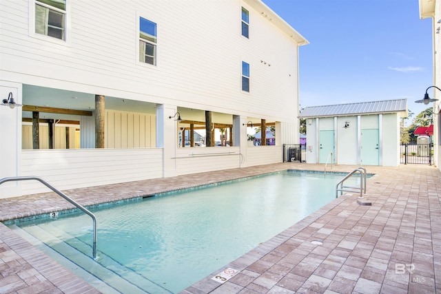 pool with a patio, an outbuilding, and fence