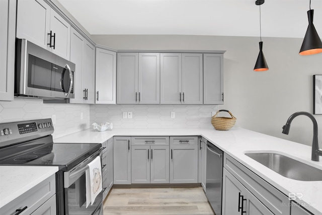 kitchen with light wood-type flooring, gray cabinets, backsplash, a sink, and appliances with stainless steel finishes