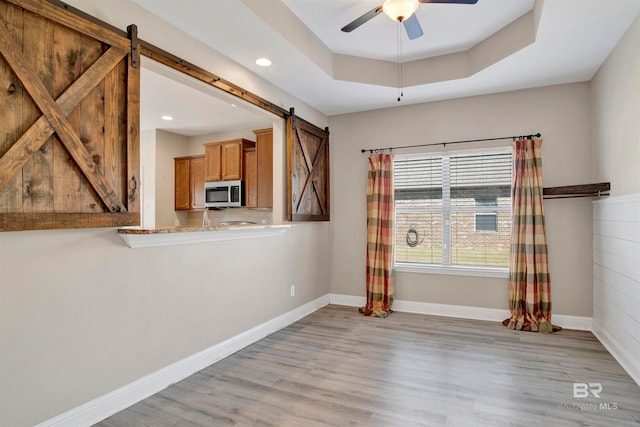 unfurnished room with light hardwood / wood-style flooring, a barn door, a tray ceiling, and ceiling fan