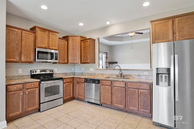 kitchen with appliances with stainless steel finishes, sink, ceiling fan, light stone counters, and light tile patterned floors