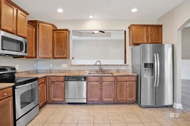 kitchen with sink, appliances with stainless steel finishes, light stone counters, and ceiling fan