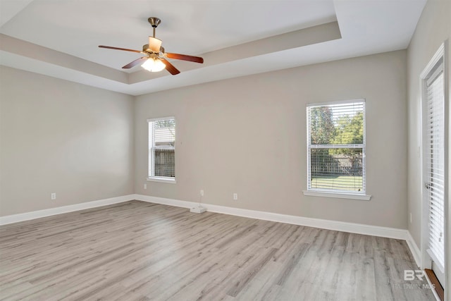 empty room featuring light hardwood / wood-style floors, a tray ceiling, and ceiling fan