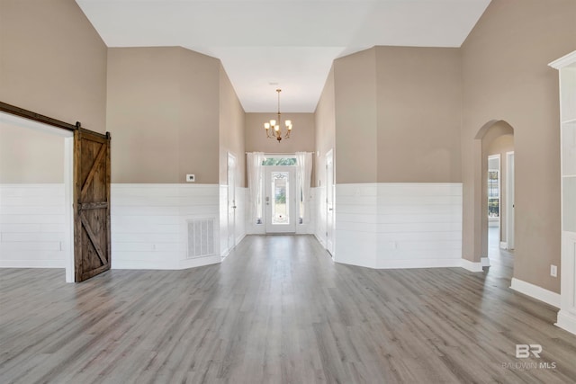 foyer with an inviting chandelier, a barn door, high vaulted ceiling, and light wood-type flooring