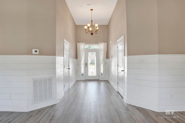 entryway with light hardwood / wood-style floors, a towering ceiling, and a chandelier