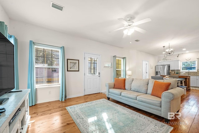 living room with ceiling fan with notable chandelier, sink, and light wood-type flooring