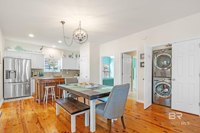 dining room featuring an inviting chandelier, stacked washer / drying machine, sink, and light wood-type flooring