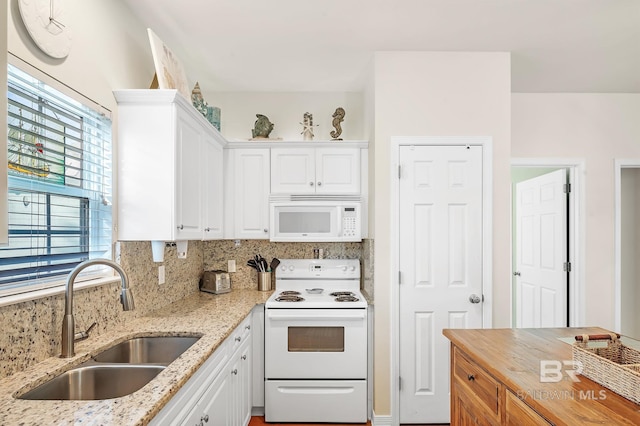 kitchen with white cabinetry, white appliances, light stone countertops, and sink