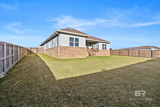 back of property with a yard, a fenced backyard, brick siding, and roof with shingles