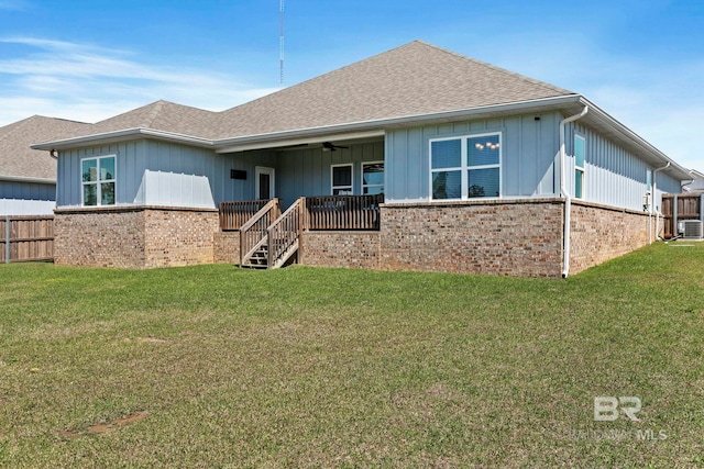 rear view of property with a yard, brick siding, roof with shingles, and fence