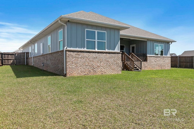 rear view of property featuring a yard, a fenced backyard, a shingled roof, board and batten siding, and brick siding