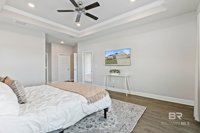 bedroom featuring a raised ceiling, wood finished floors, visible vents, and baseboards