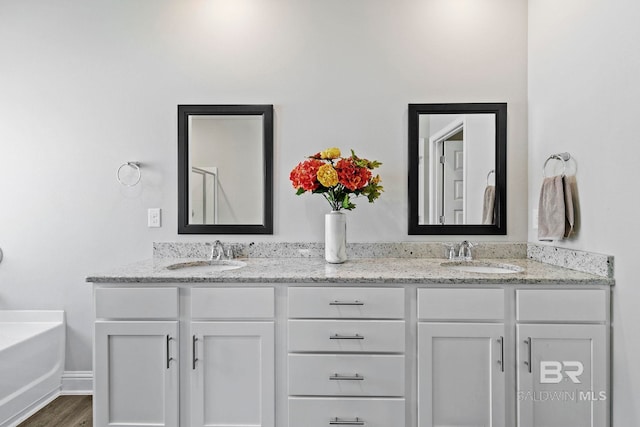 full bath with double vanity, wood finished floors, a tub, and a sink