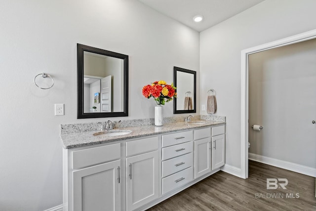 full bath with a sink, baseboards, wood finished floors, and double vanity