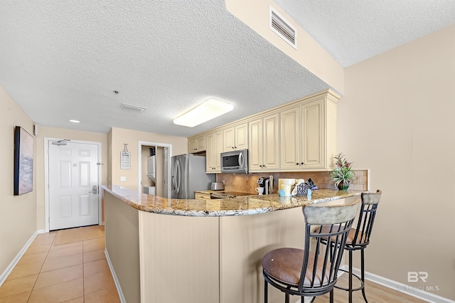 527 Beach Club Trl Unit C305, Gulf Shores, AL 36542 - kitchen with a peninsula, visible vents, cream cabinetry, light stone countertops, and appliances with stainless steel finishes