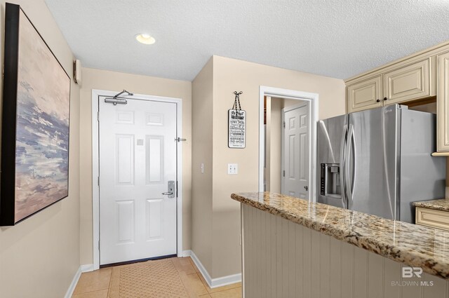 527 Beach Club Trl Unit C305, Gulf Shores, AL 36542 - kitchen featuring cream cabinetry, light tile patterned floors, light stone countertops, baseboards, and stainless steel fridge
