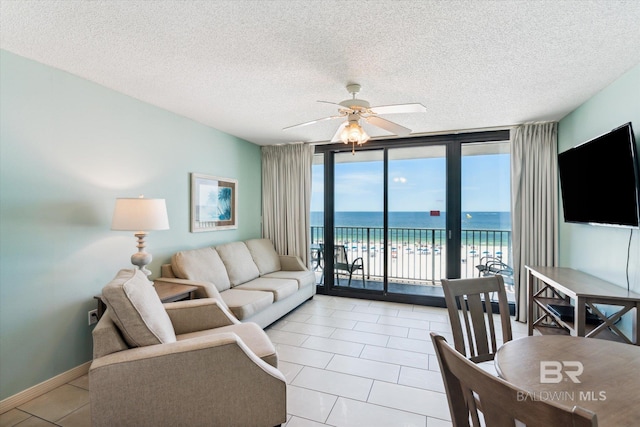 tiled living room featuring a water view, expansive windows, ceiling fan, a view of the beach, and a textured ceiling