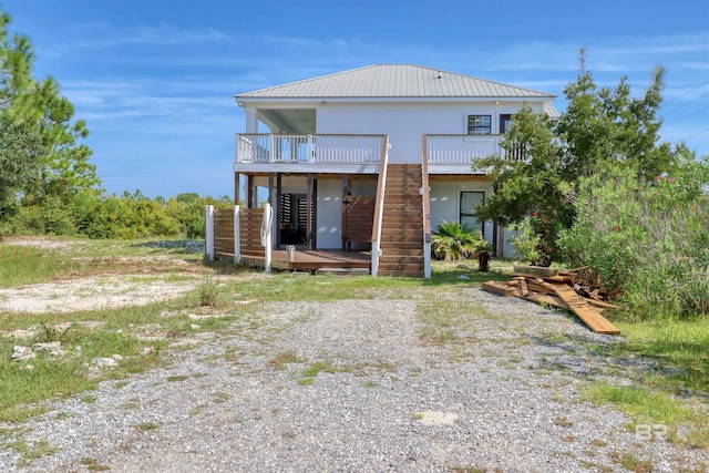 rear view of property featuring metal roof, stairs, stucco siding, and a deck