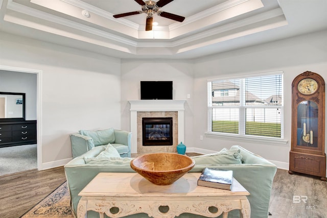 living room with ceiling fan, a raised ceiling, ornamental molding, and light wood-type flooring