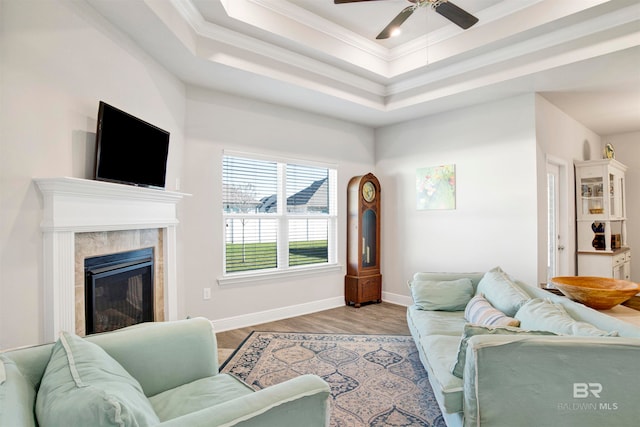 living room with light hardwood / wood-style floors, a raised ceiling, ceiling fan, and ornamental molding