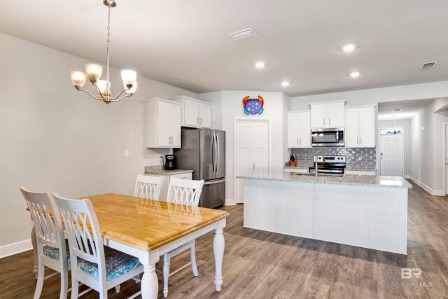 kitchen with hanging light fixtures, light stone counters, wood-type flooring, white cabinets, and appliances with stainless steel finishes