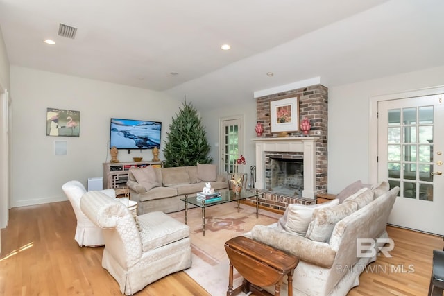 living room featuring a brick fireplace, vaulted ceiling, and light wood-type flooring