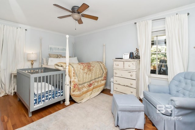 bedroom featuring ceiling fan, crown molding, a crib, and light wood-type flooring