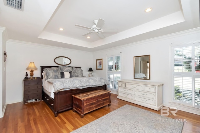 bedroom featuring hardwood / wood-style flooring, ceiling fan, a raised ceiling, and multiple windows